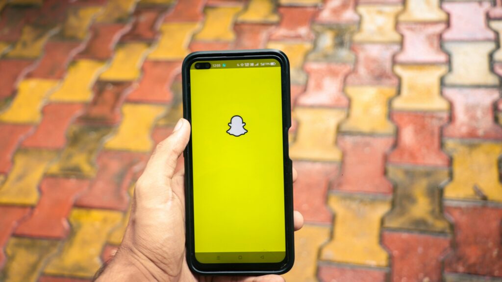 Dodatki do Snapchata – smartfon z włączoną aplikacją Snapchat na kolorowej kostce brukowej, trzymany w dłoni, jasny żółty ekran z ikoną ducha